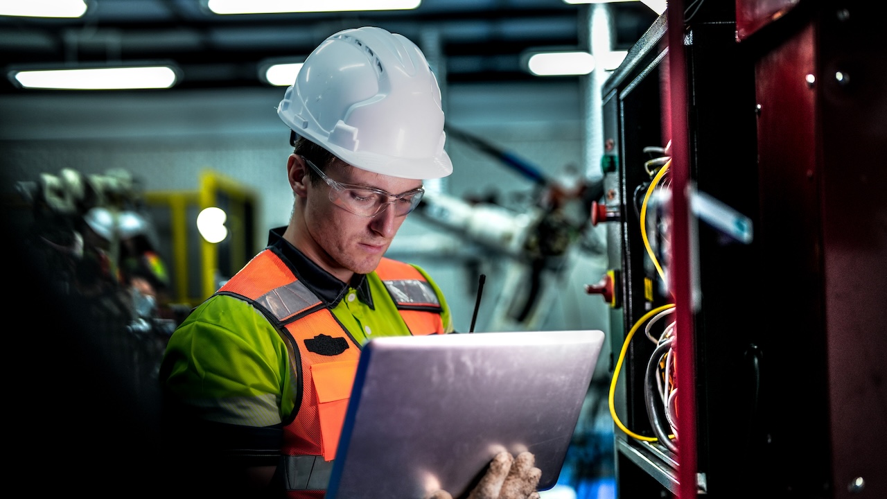 An engineer represents the future of work, using a laptop to manage AI and robotics. This high-tech automation optimizes the manufacturing supply chain.